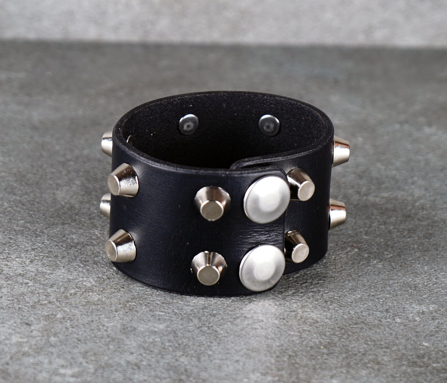 Black leather bracelet with silver studs on a gray surface