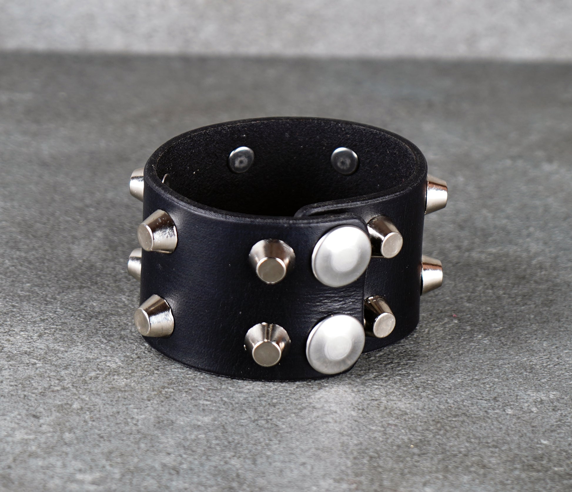 Black leather bracelet with silver studs on a gray surface