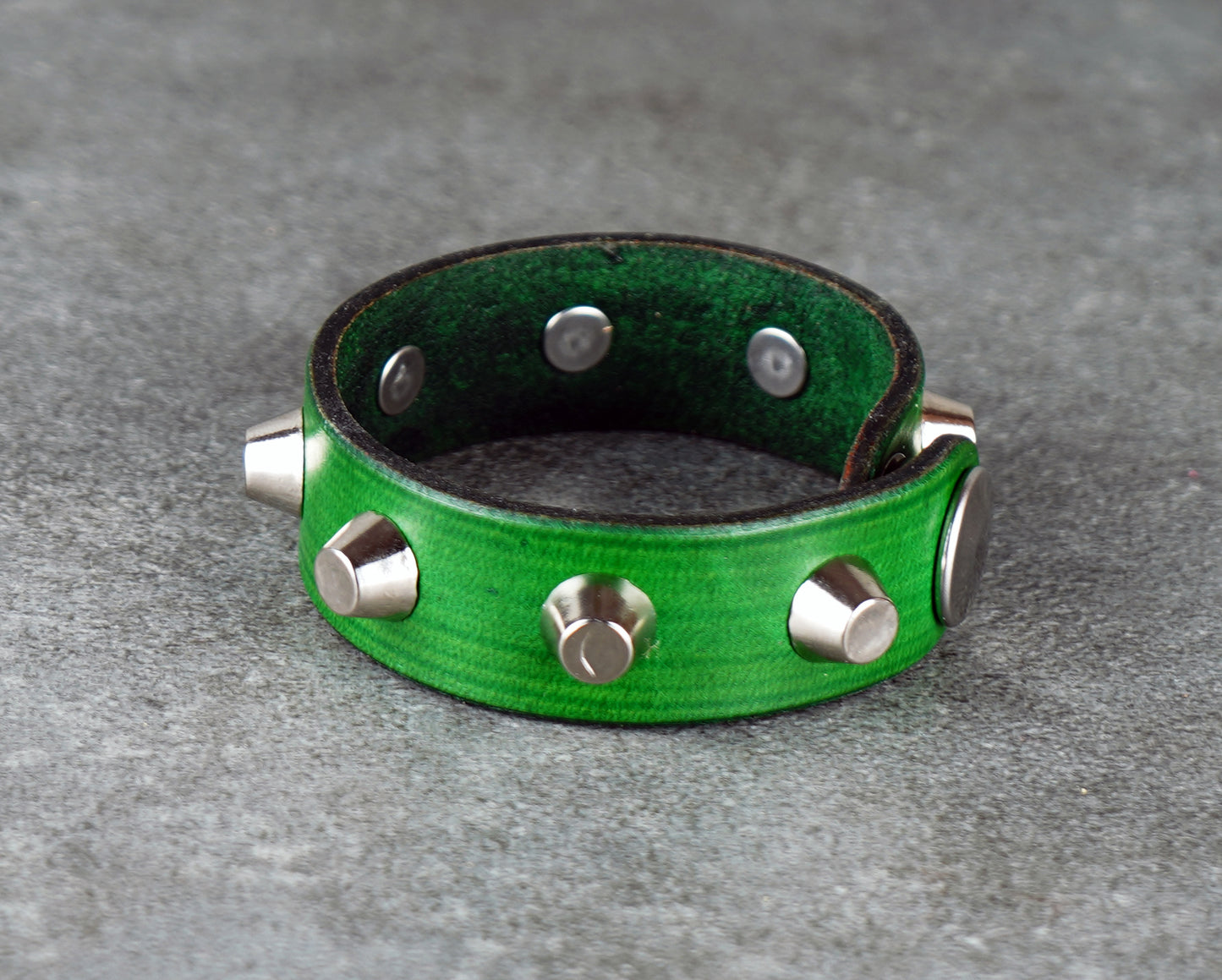 Green leather bracelet with silver studs on a gray surface