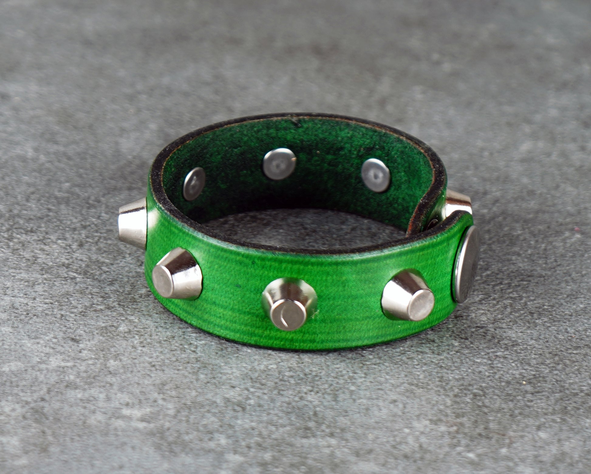 Green leather bracelet with silver studs on a gray surface