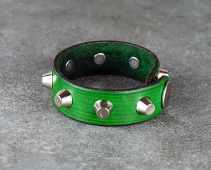 Green leather bracelet with silver studs on a gray surface