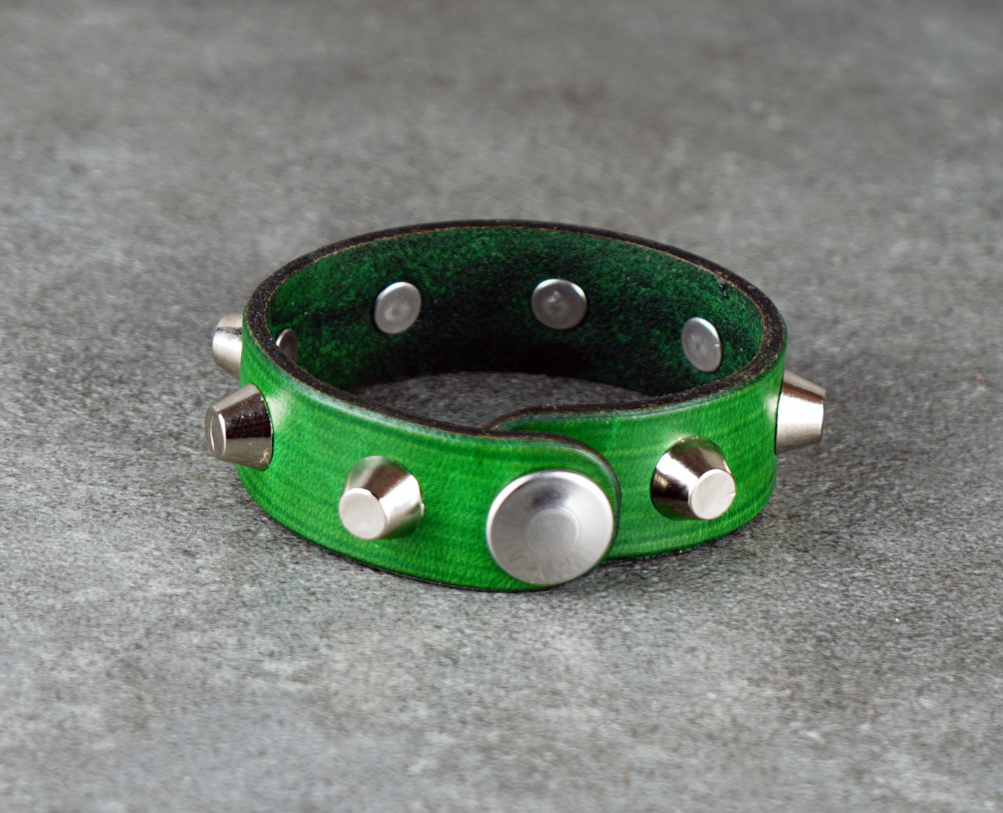 Green leather bracelet with silver studs on a gray surface