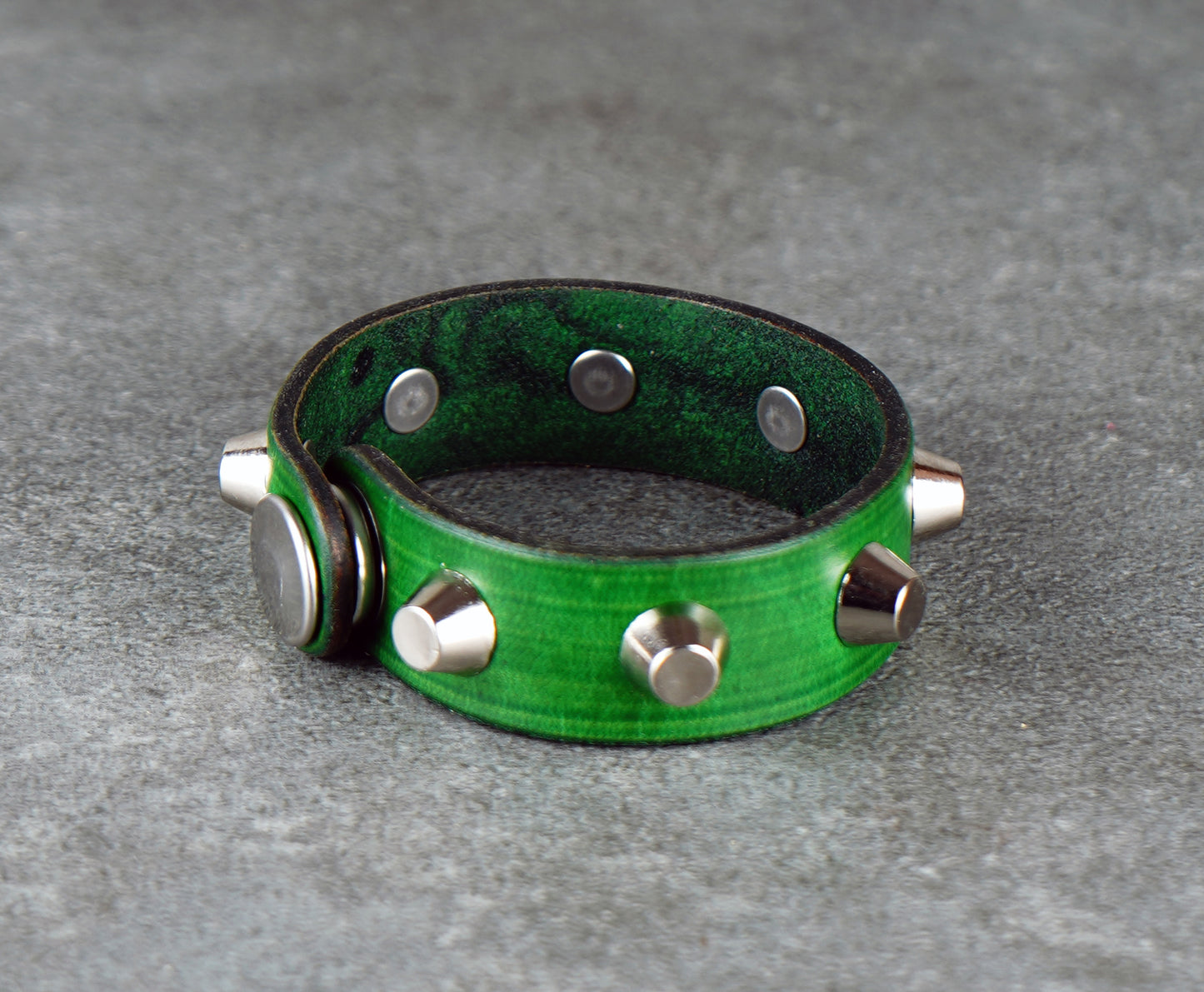 Green leather bracelet with silver studs on a gray surface