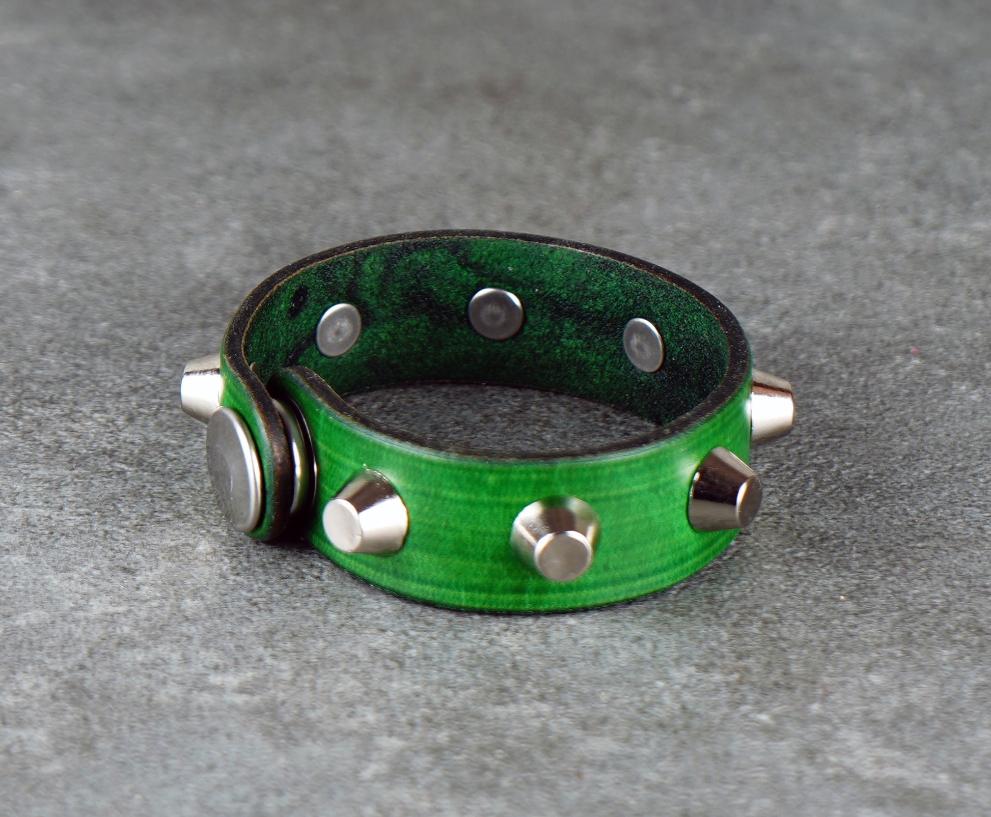 Green leather bracelet with silver studs on a gray surface