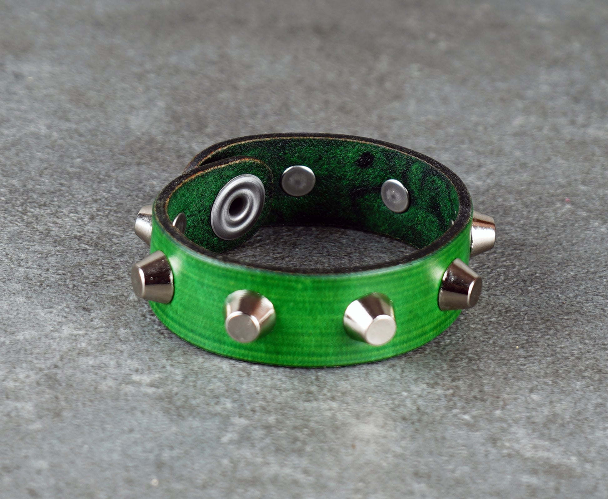 Green leather bracelet with metallic studs on a gray surface