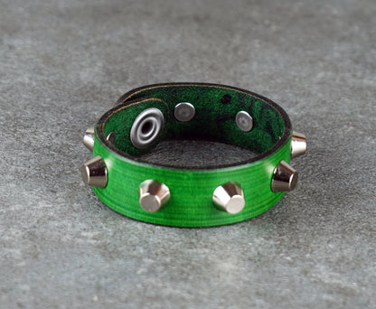 Green leather bracelet with metallic studs on a gray surface