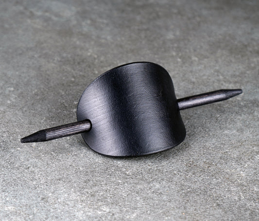 Black oval leather barrette with a wooden stick passing through it on a gray surface