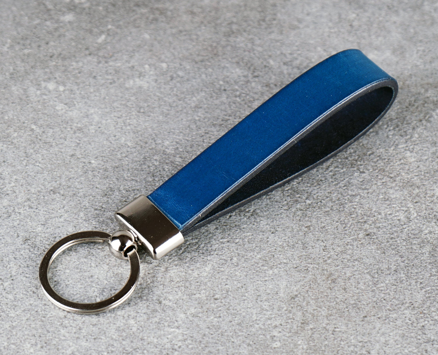 Blue leather keychain with silver key ring on a gray surface