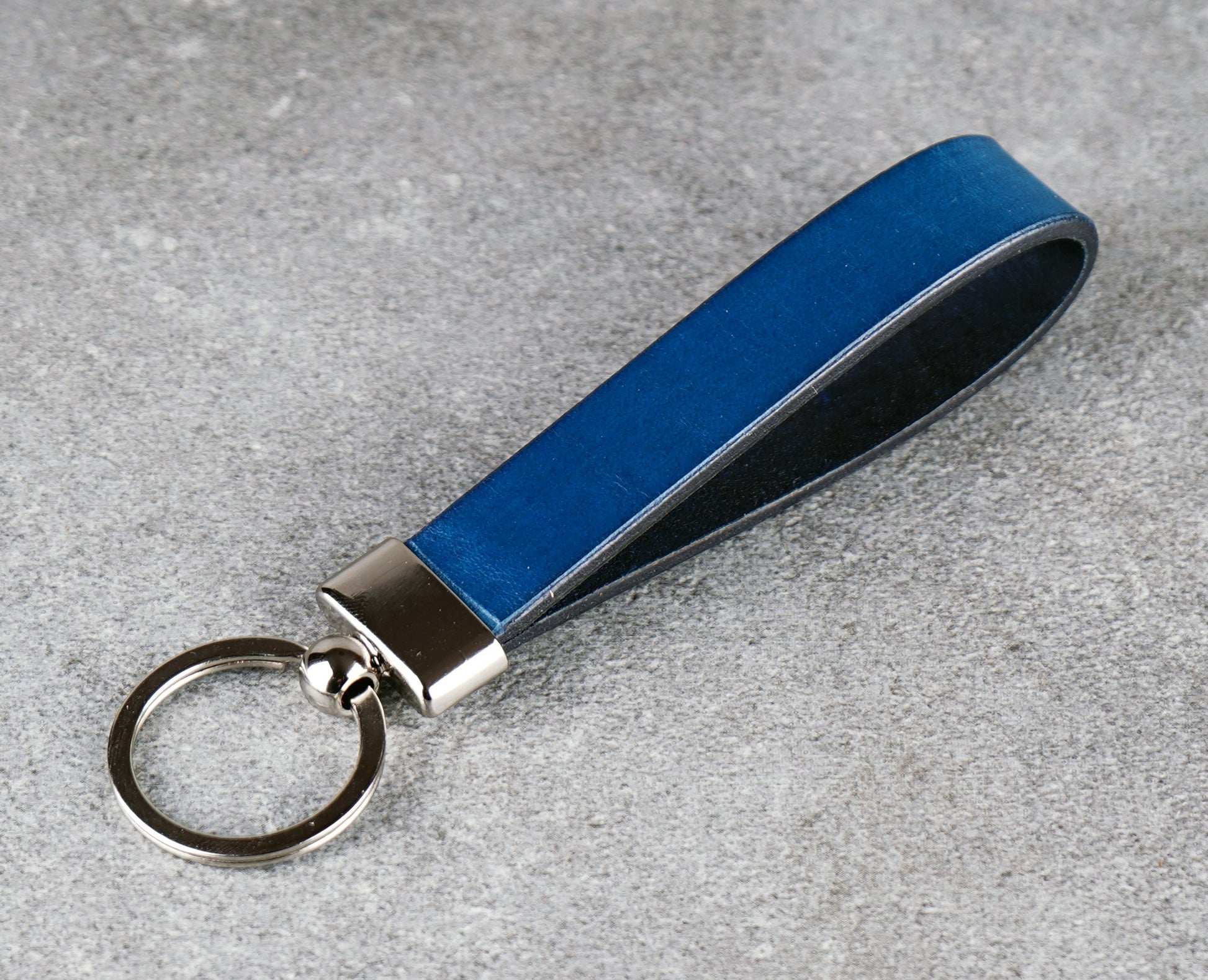 Blue leather keychain with silver key ring on a gray surface