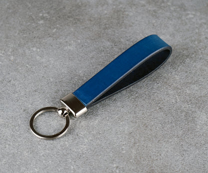 Blue leather keychain with silver key ring on a gray concrete surface