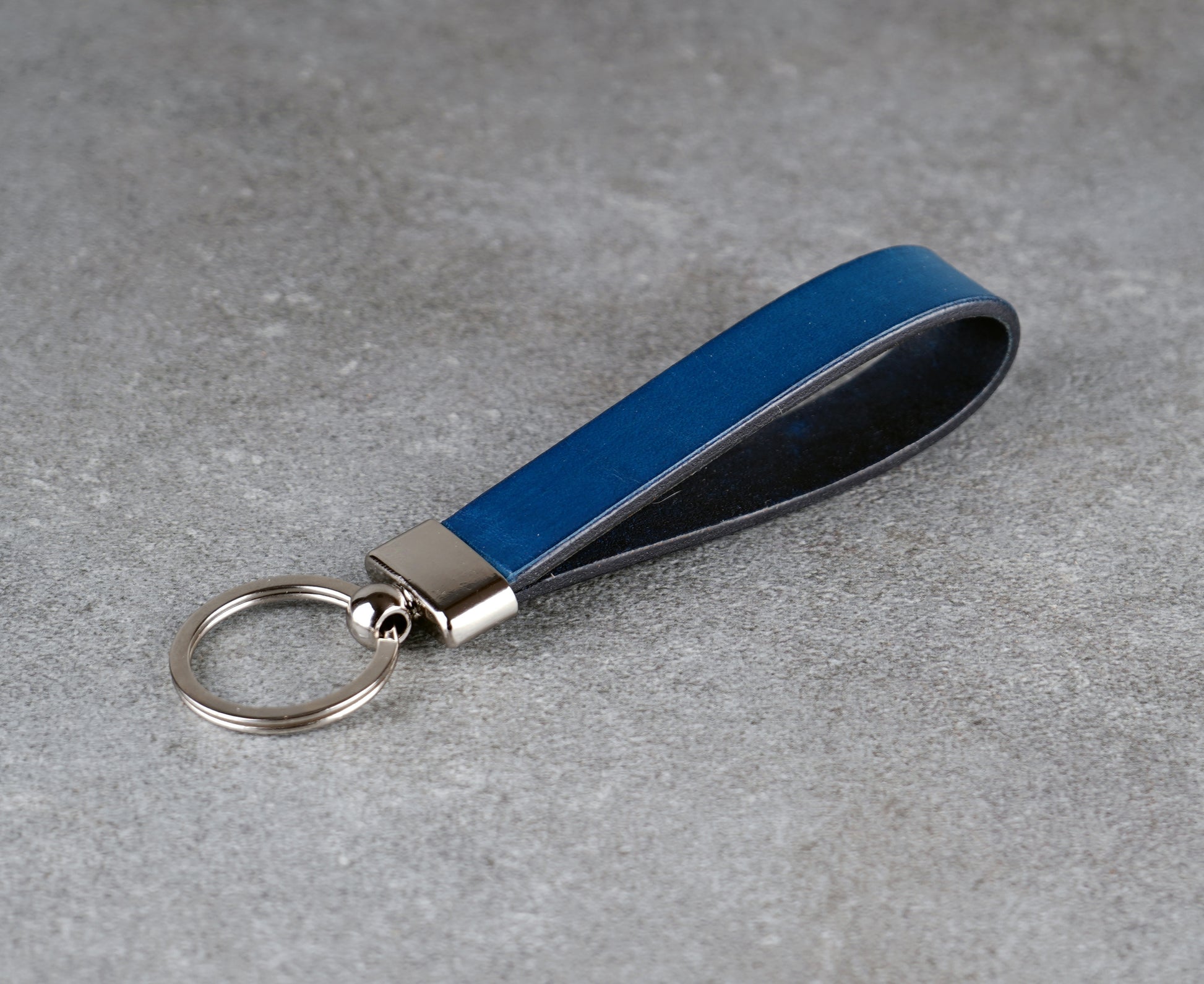 Blue leather keychain with silver ring on a gray surface