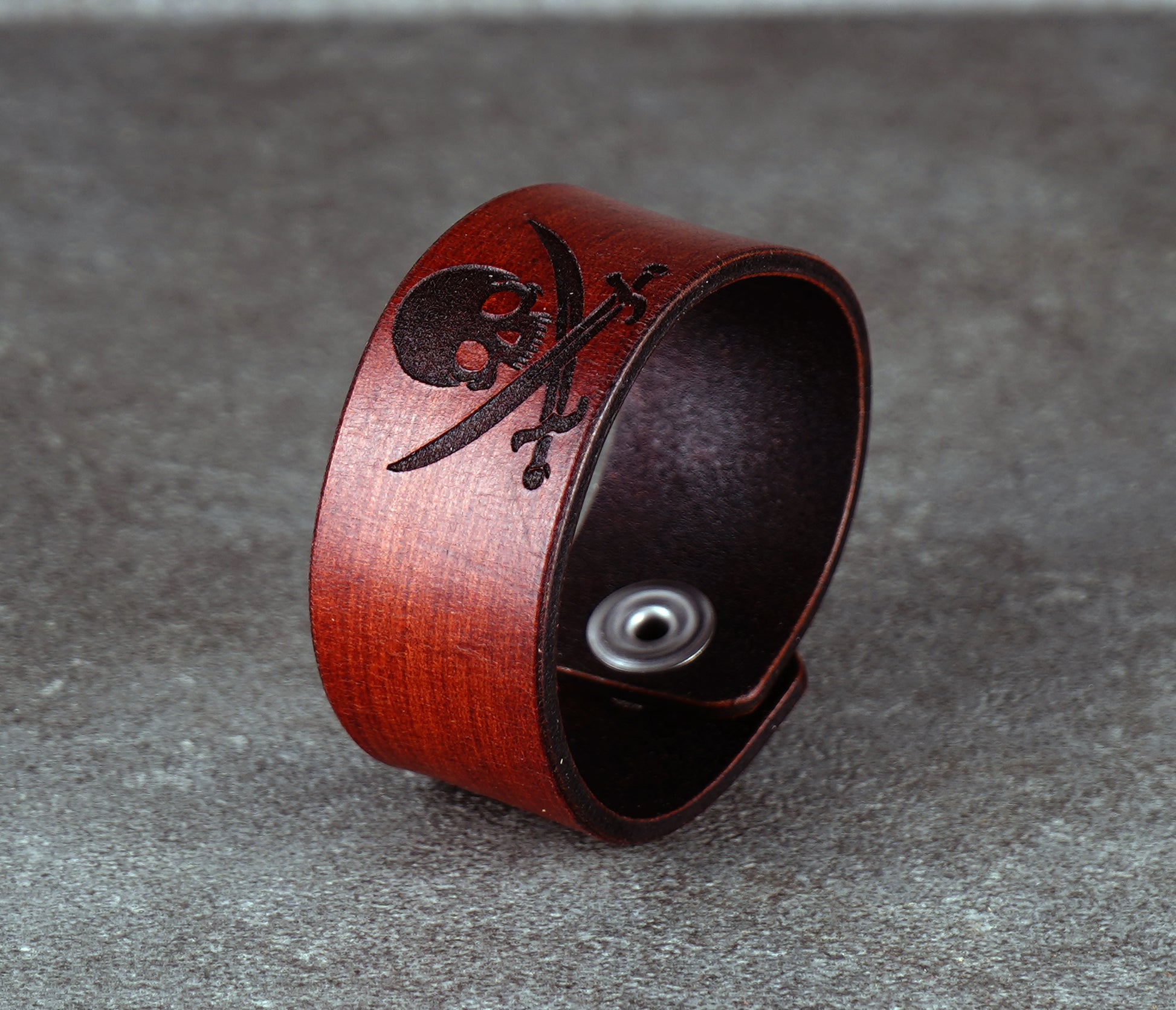 Brown leather bracelet with skull and crossbones design on a gray surface