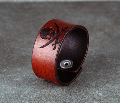 Brown leather bracelet with skull and crossbones design on a gray surface