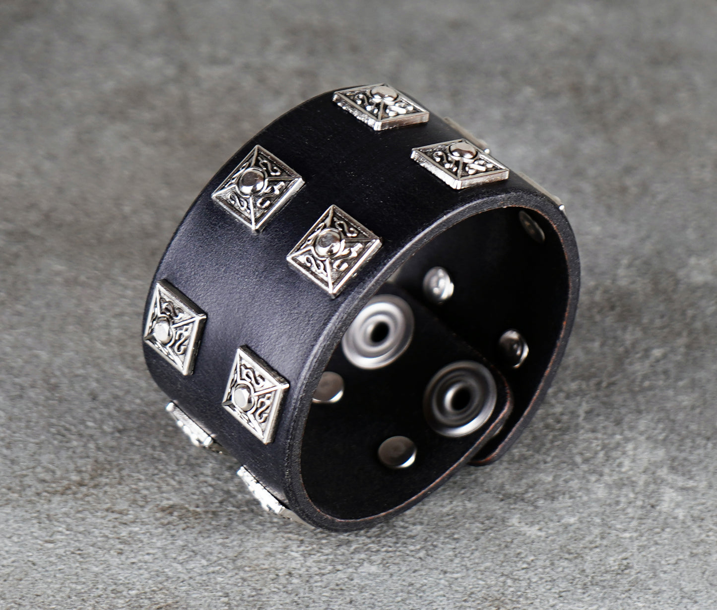 Black leather bracelet with silver metal studs on a gray surface