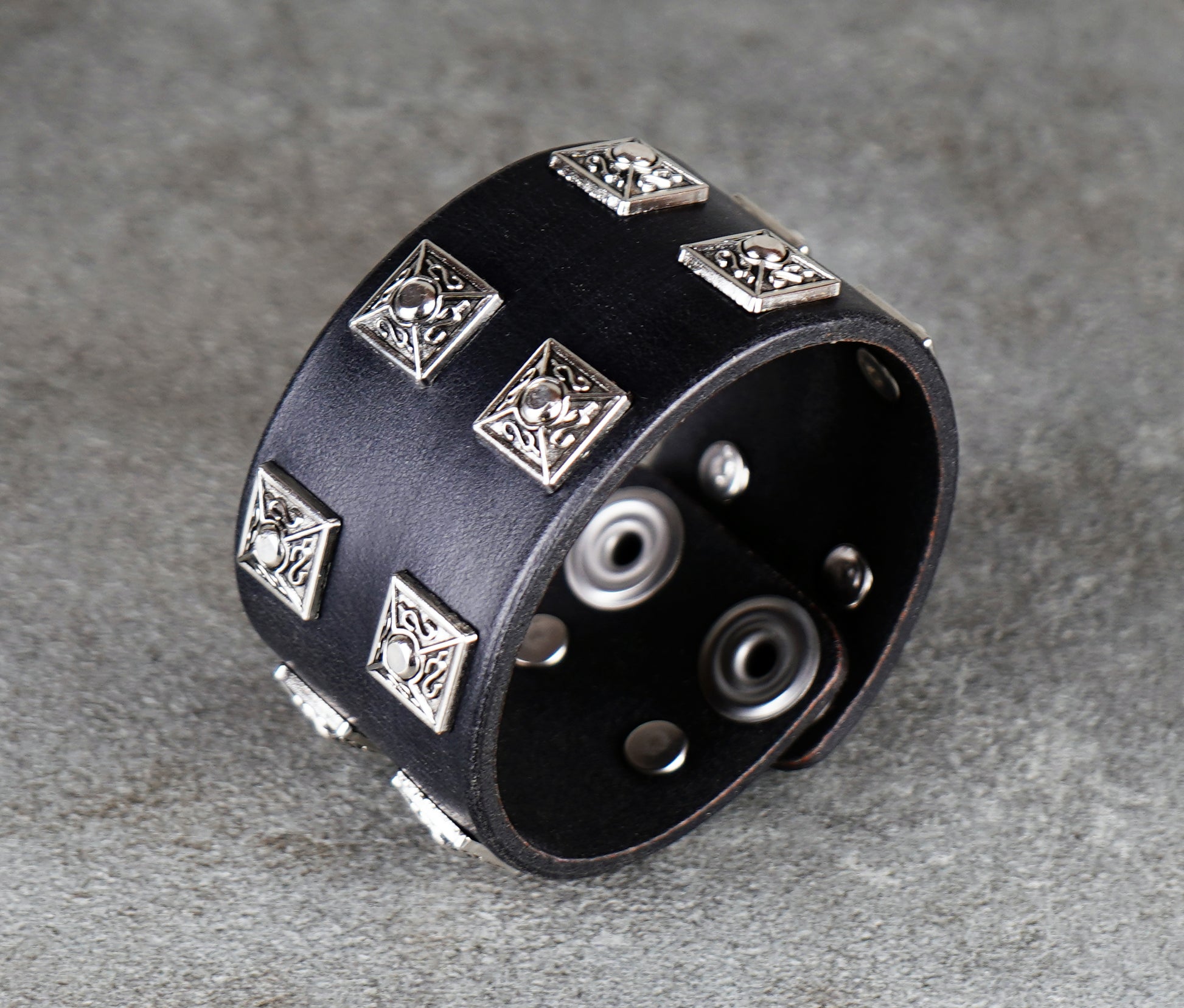 Black leather bracelet with silver metal studs on a gray surface