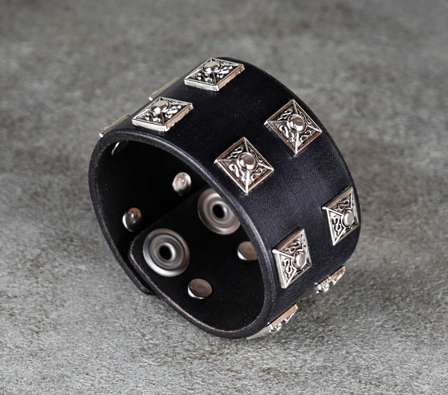 Black leather cuff bracelet with silver geometric studs on a gray background
