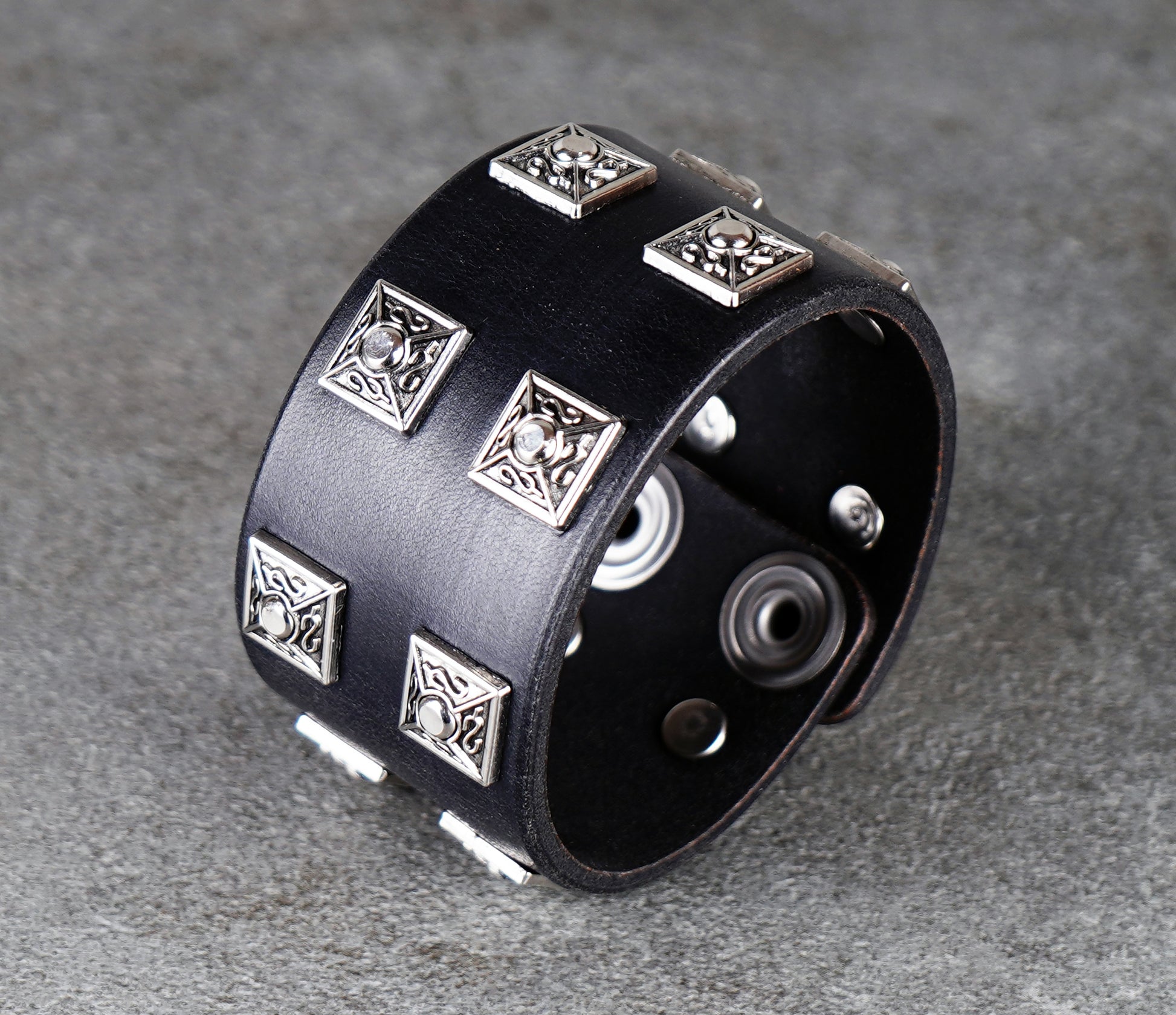 Black leather cuff bracelet with silver geometric studs on a gray background
