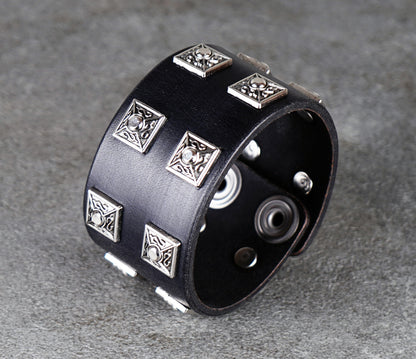 Black leather cuff bracelet with silver geometric studs on a gray background
