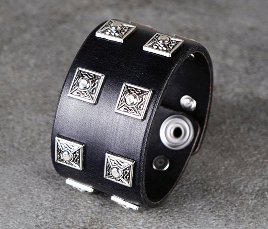 Black leather cuff bracelet with silver geometric studs on a gray background