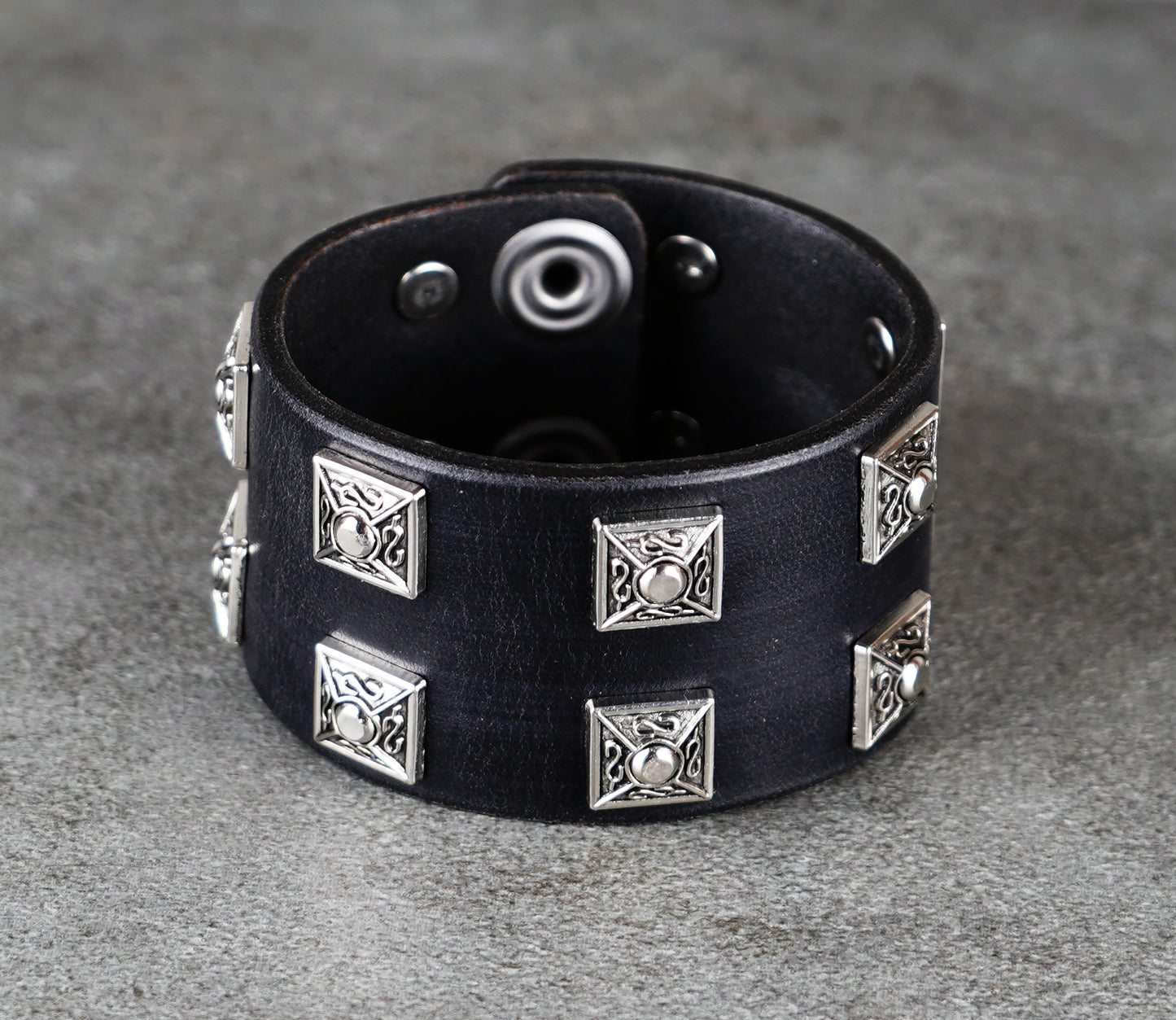 Black leather bracelet with silver geometric studs on a gray surface