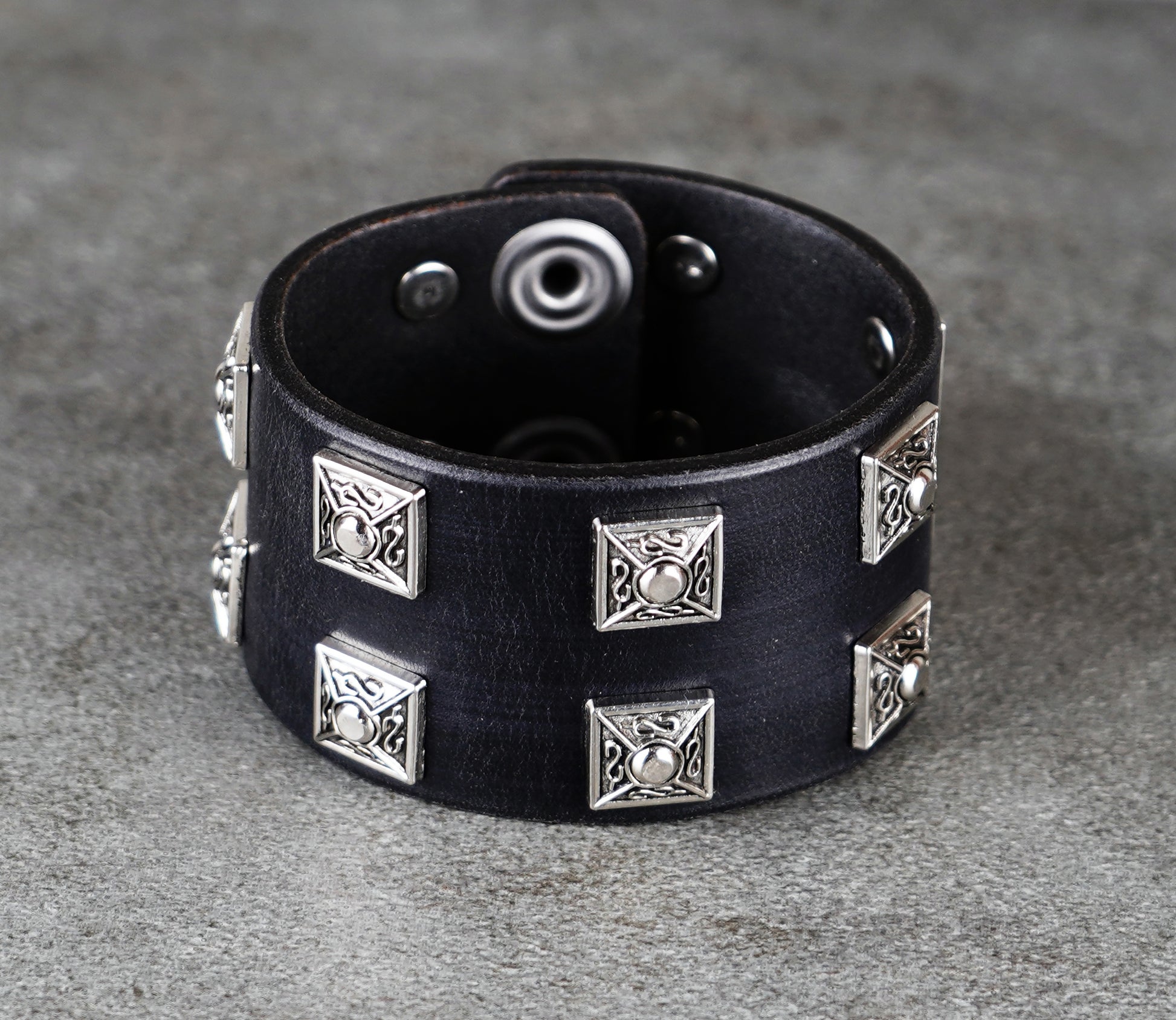 Black leather bracelet with silver geometric studs on a gray surface