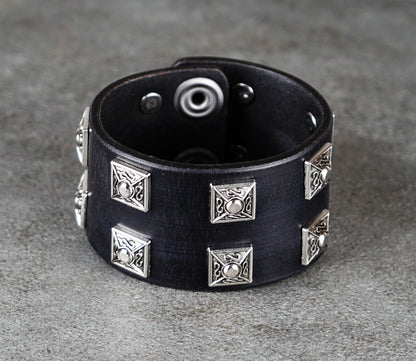 Black leather bracelet with silver geometric studs on a gray surface