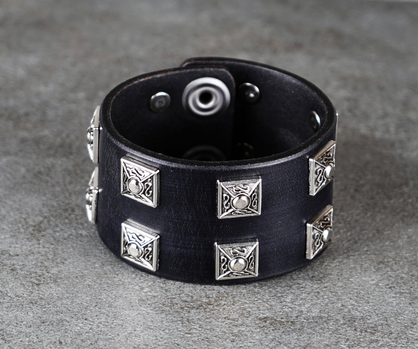 Black leather bracelet with silver studs on a gray surface