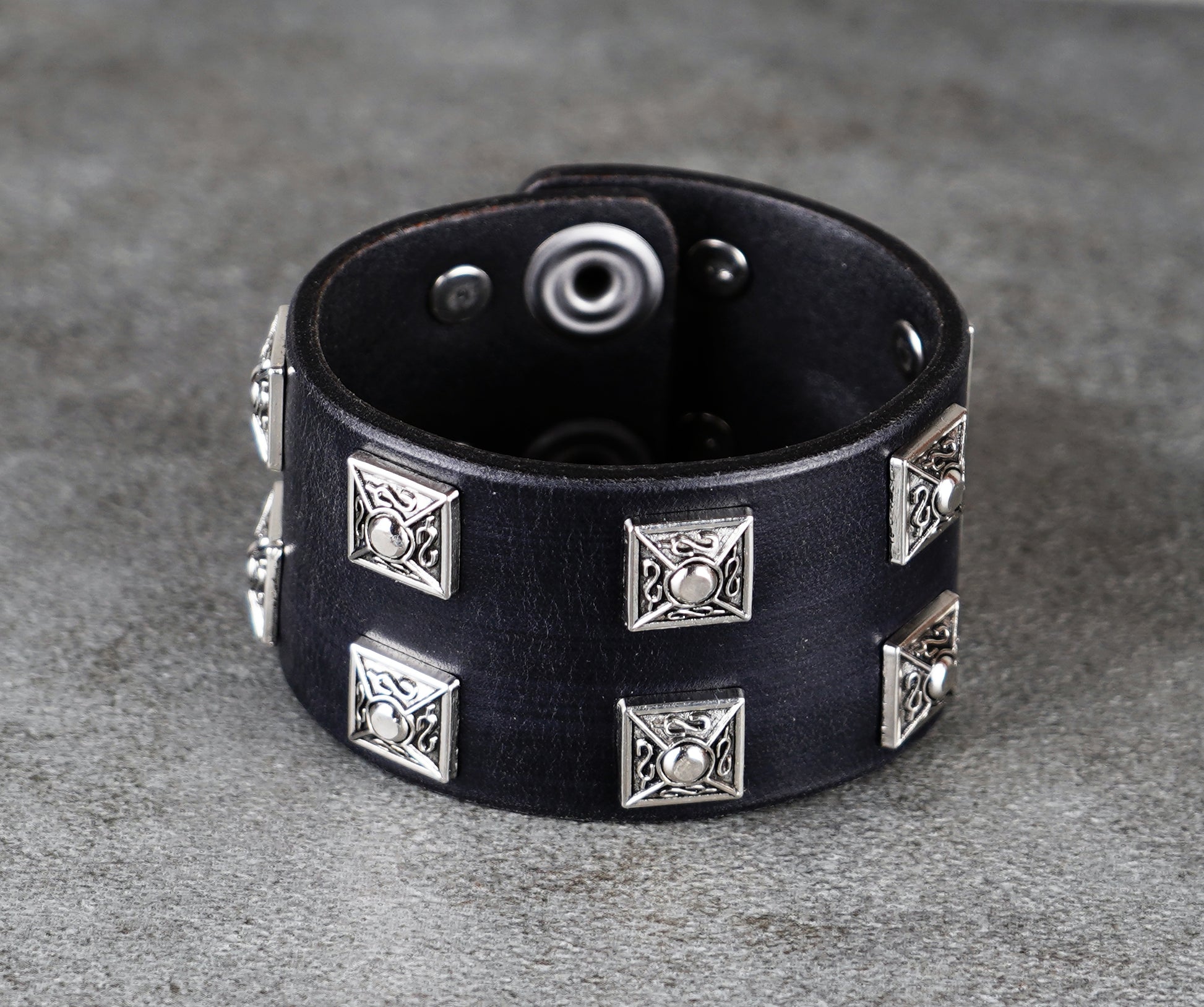 Black leather bracelet with silver studs on a gray surface