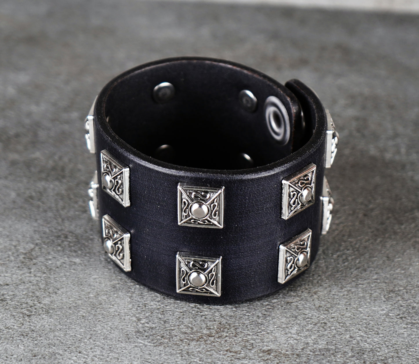 Black leather bracelet with silver studs on a gray surface
