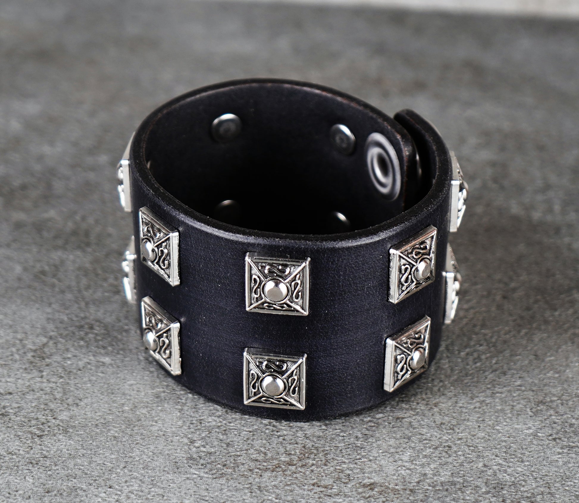 Black leather bracelet with silver studs on a gray surface