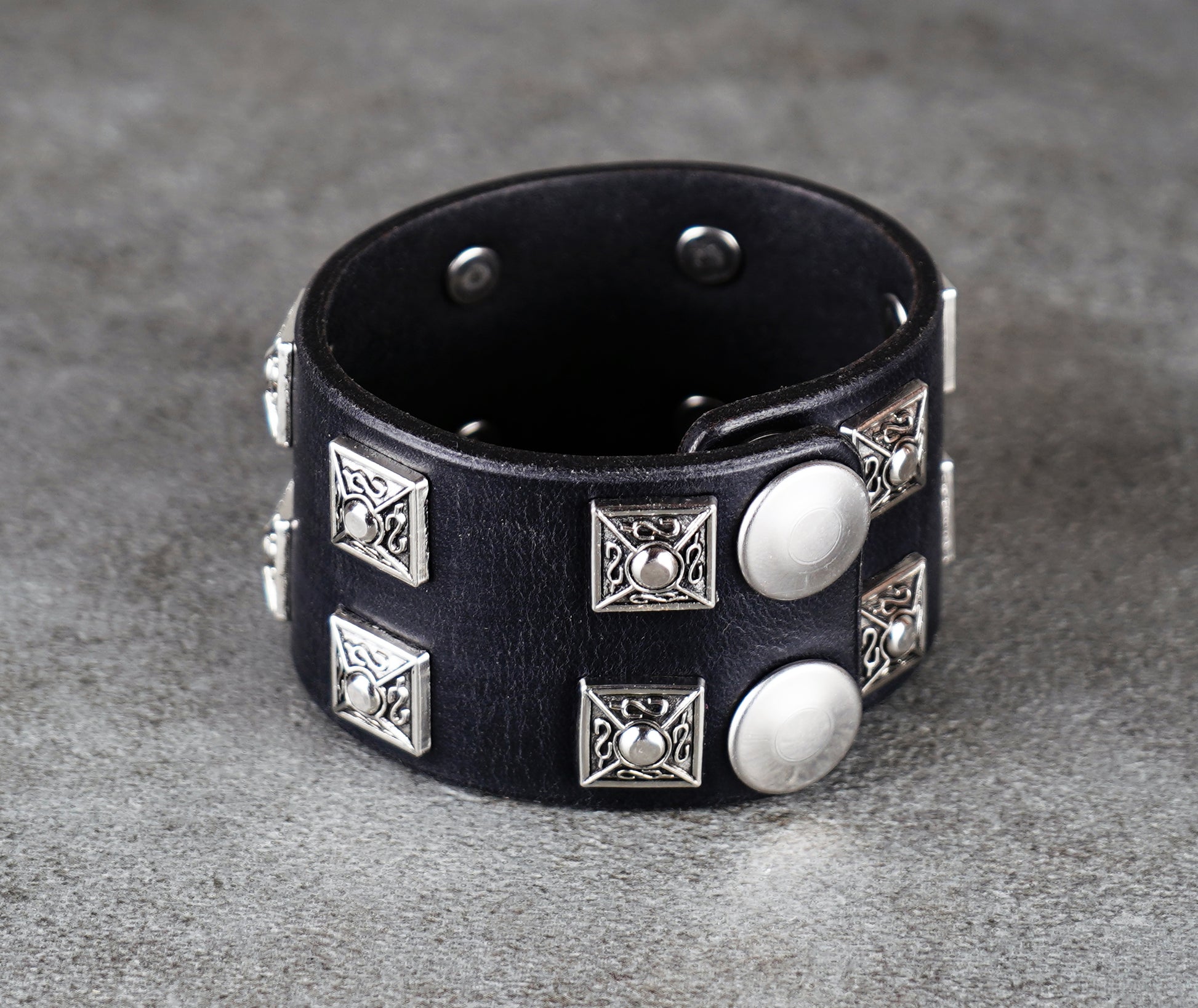 Black leather bracelet with silver studs on a gray surface
