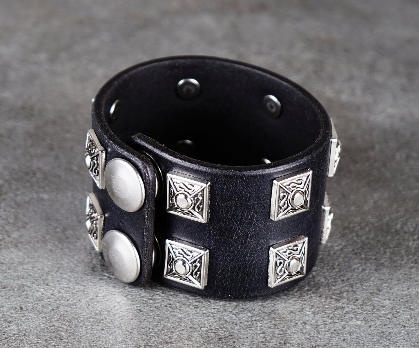 Black leather bracelet with silver studs on a gray background