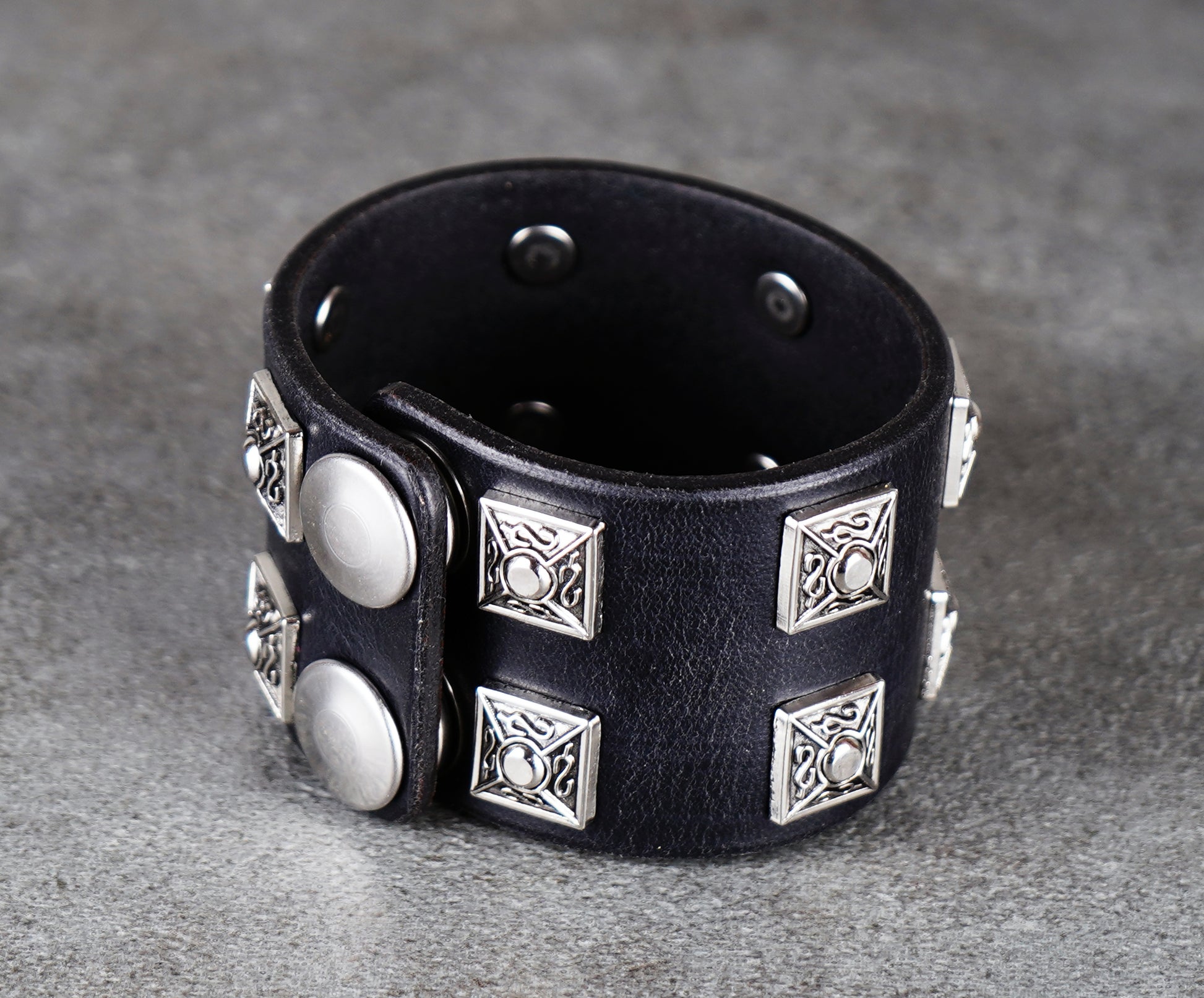 Black leather bracelet with silver studs on a gray background