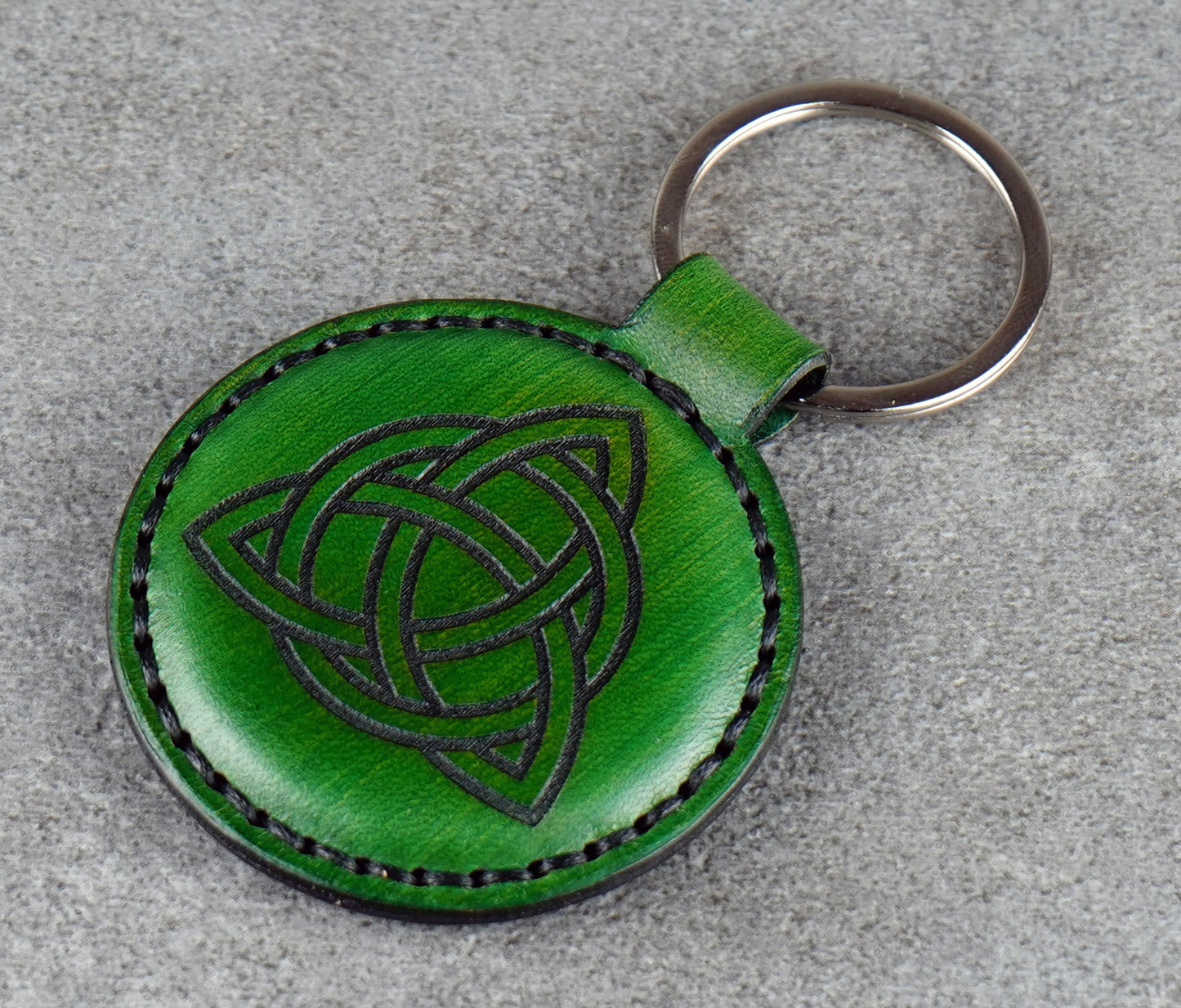Green leather keychain with Celtic knot design on a gray surface