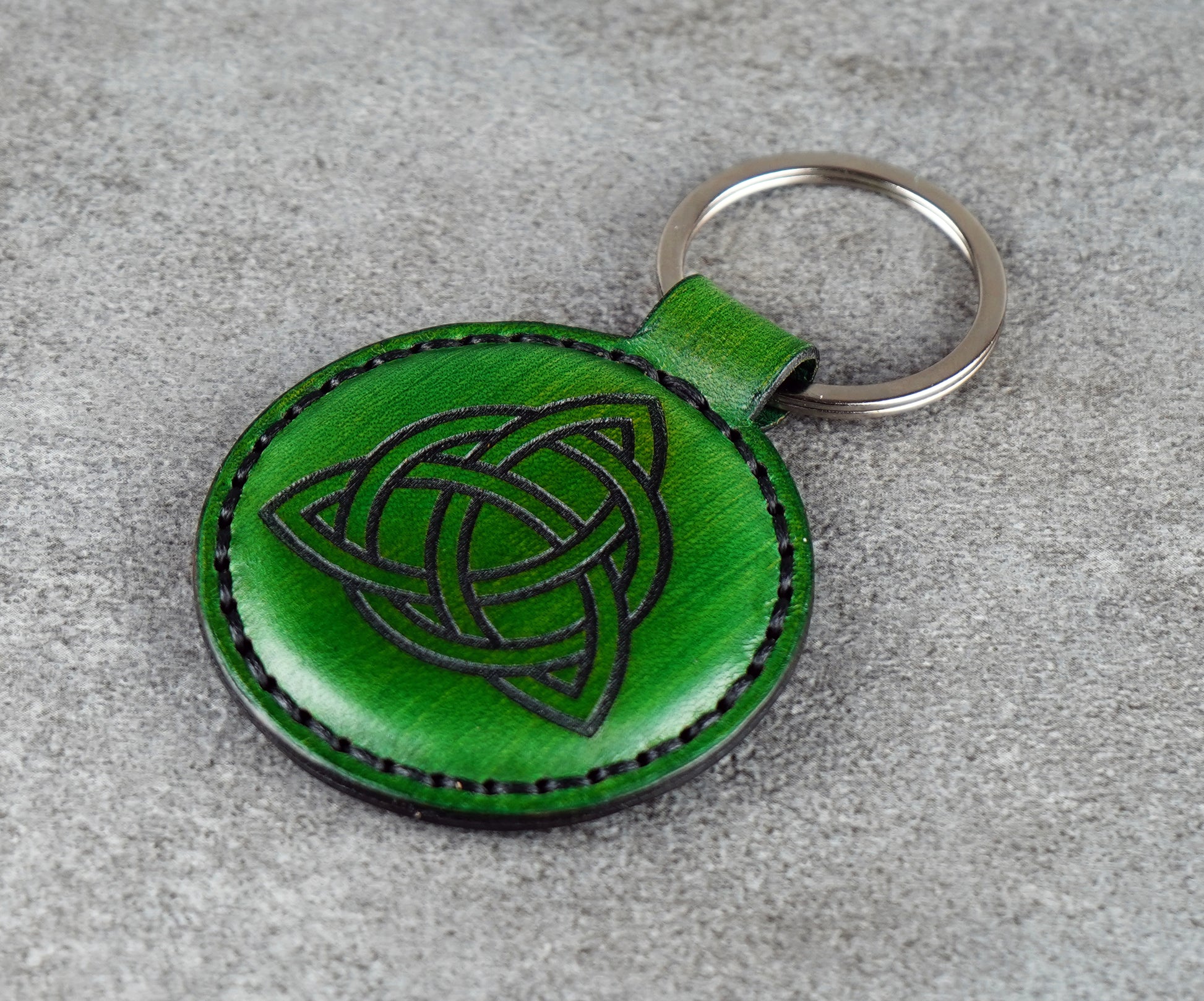 Green leather keychain with Celtic knot design on a gray surface