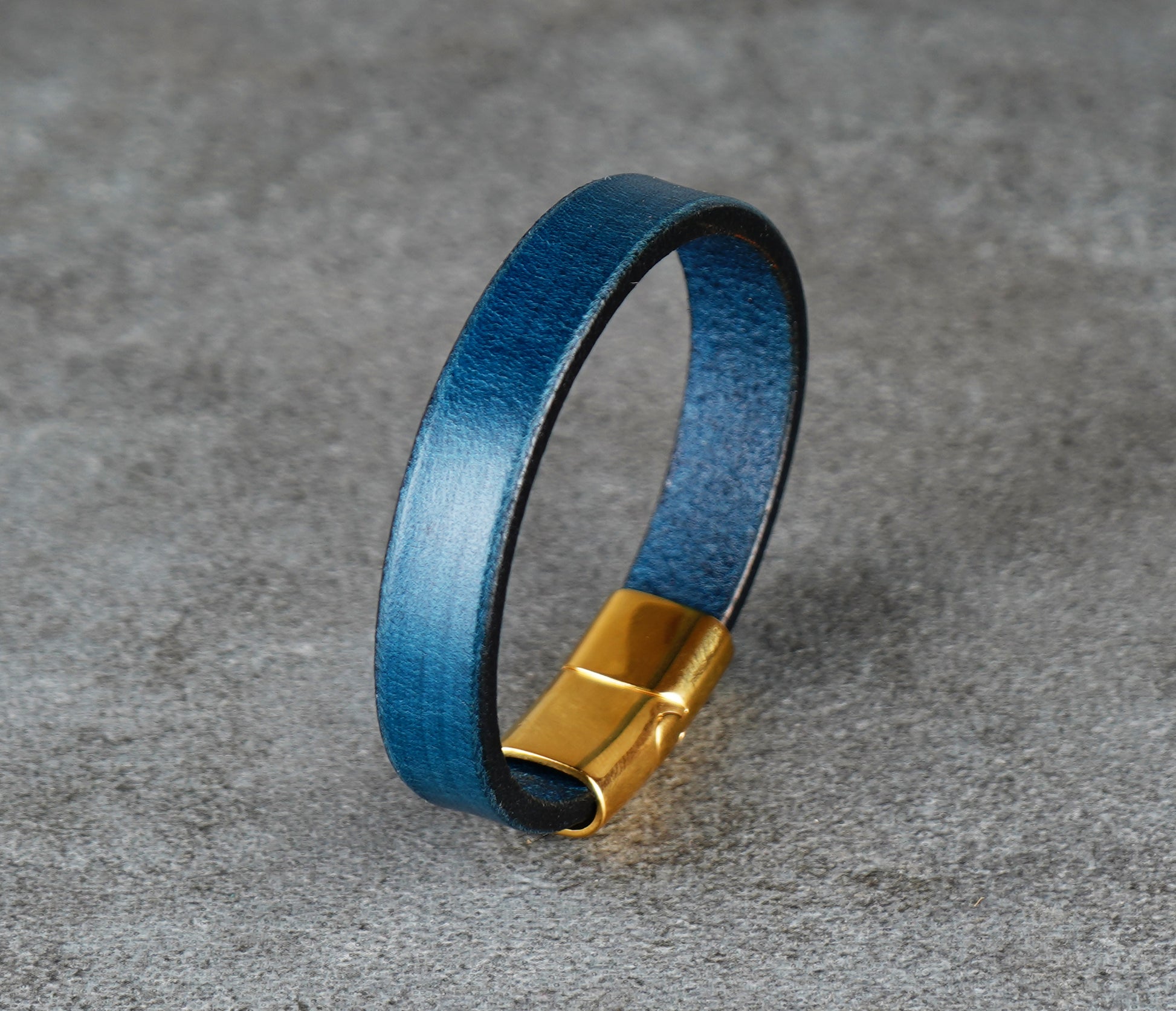 Blue leather bracelet with a gold clasp on a gray surface
