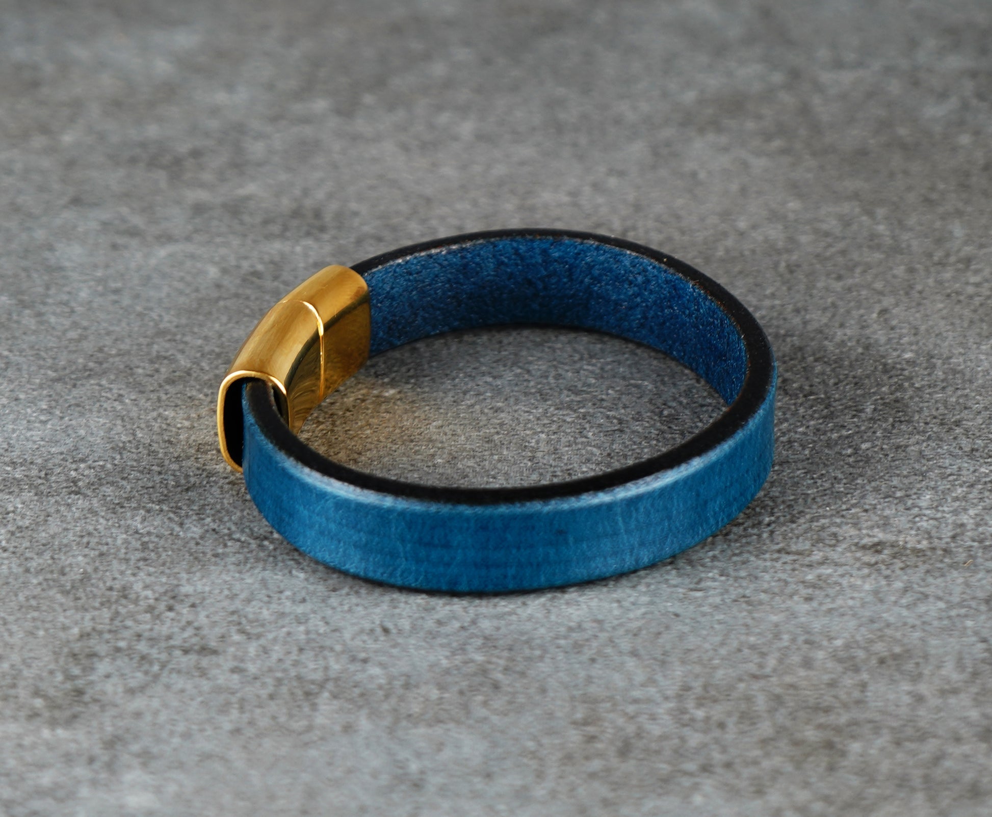 Blue leather bracelet with a gold clasp on a gray surface