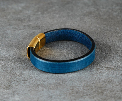Blue leather bracelet with a gold clasp on a gray surface