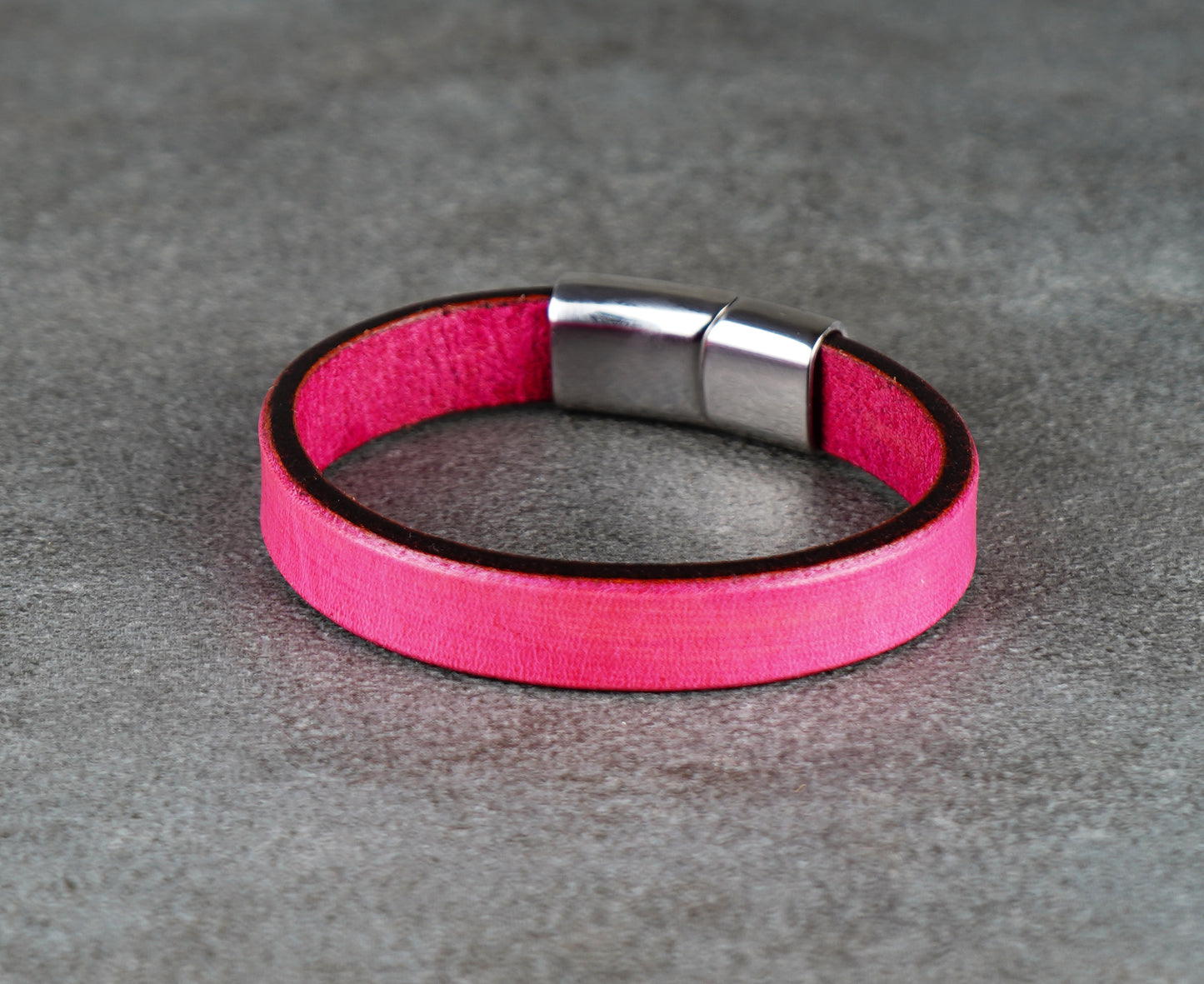 Pink leather bracelet with a silver clasp on a gray surface