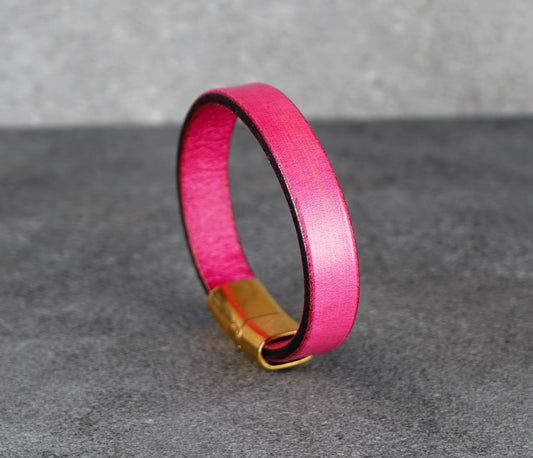 Pink leather bracelet with gold clasp on a gray surface