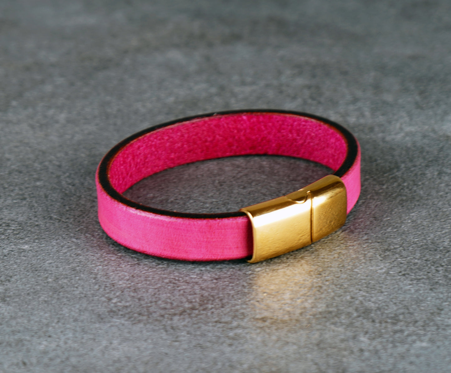 Pink leather bracelet with a gold clasp on a gray surface