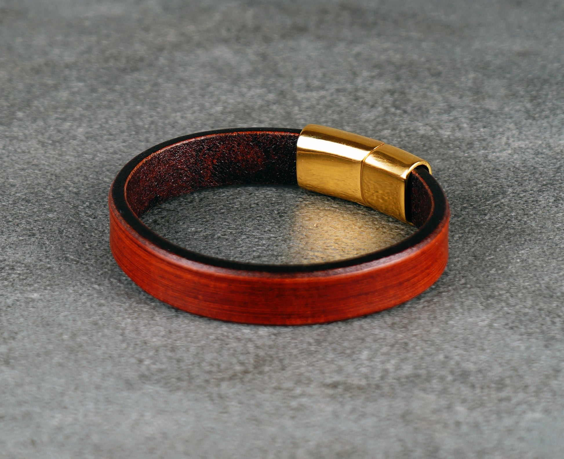 brown leather bracelet with a gold clasp on a gray surface