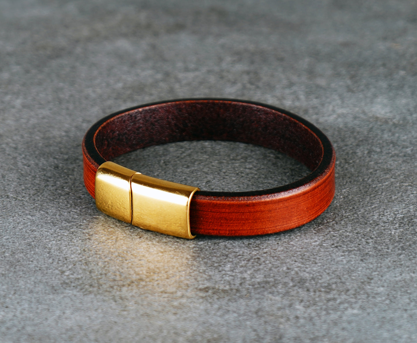 Brown leather bracelet with gold clasp on a gray surface
