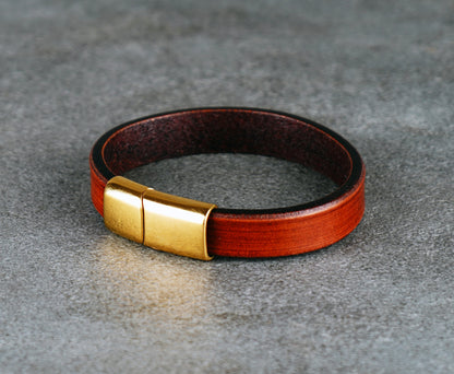 Brown leather bracelet with gold clasp on a gray surface
