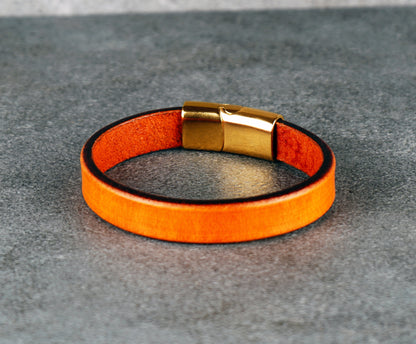 Orange leather bracelet with gold clasp on a gray surface