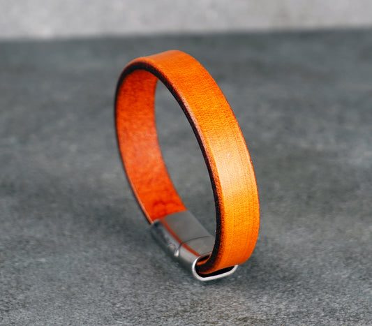 Orange leather bracelet with a metal clasp on a gray background