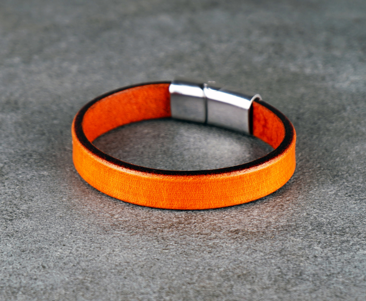 Orange leather bracelet with a silver clasp on a gray surface