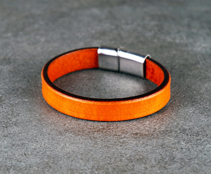 Orange leather bracelet with a silver clasp on a gray surface