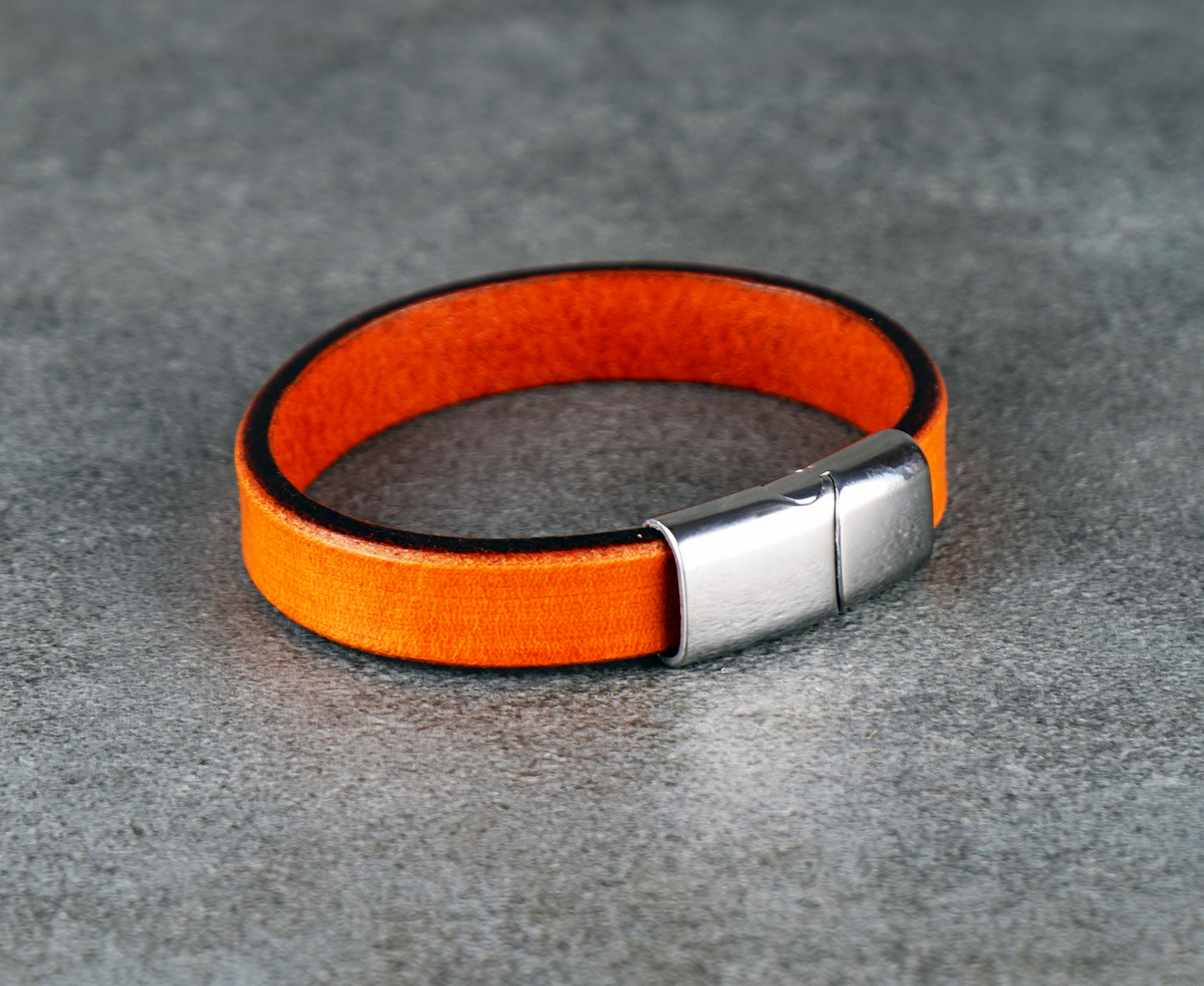 Orange leather bracelet with a silver clasp on a gray surface