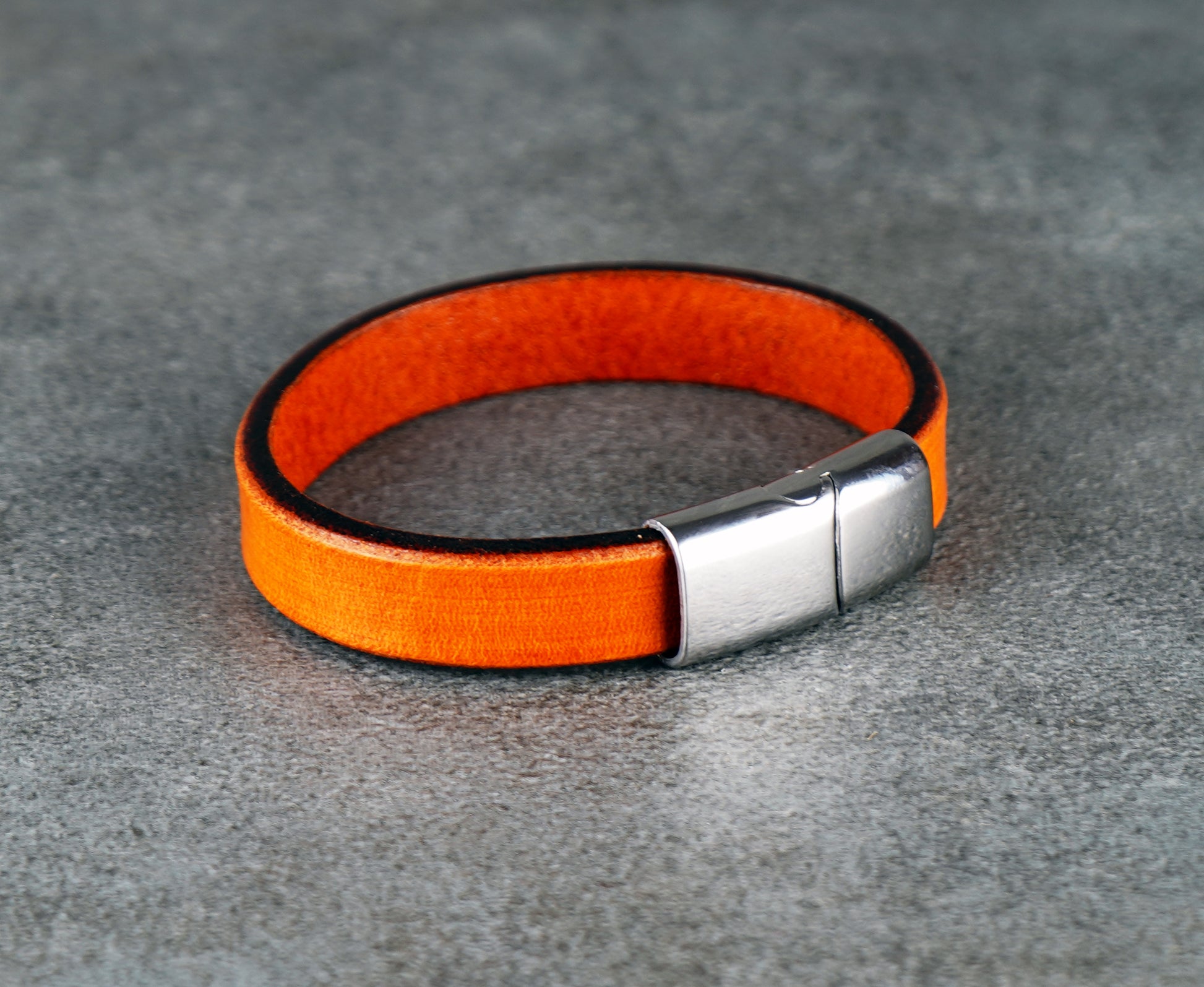 Orange leather bracelet with a silver clasp on a gray surface
